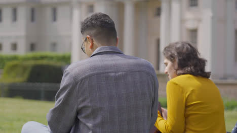 Mid-Shot-from-Behind-Two-Students-Talking-and-Working-in-Campus-Park